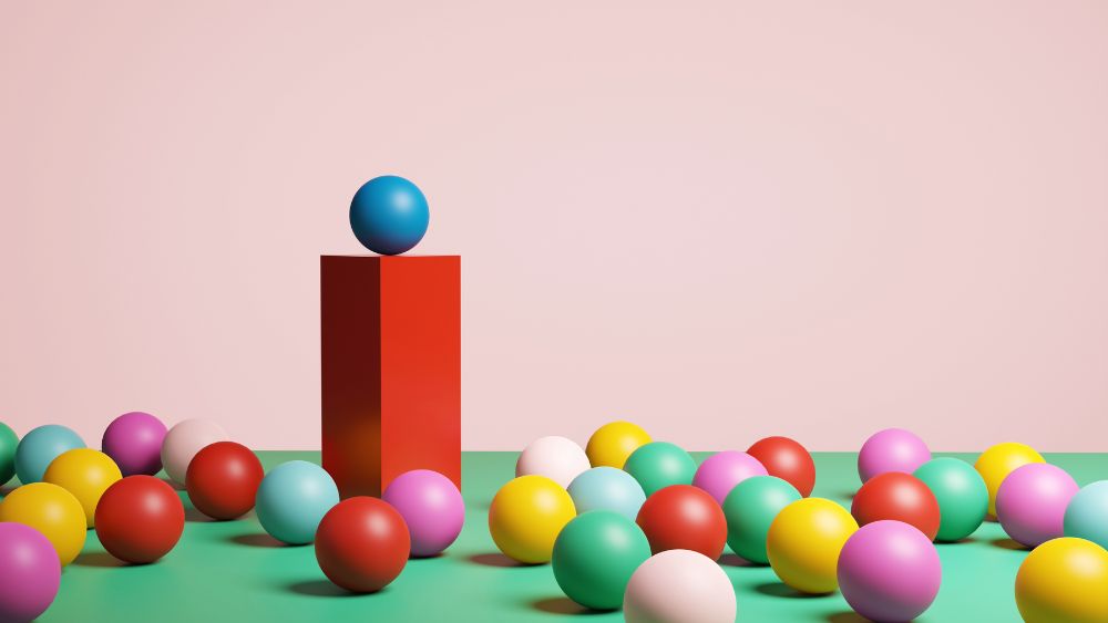 Lots of multicoloured spheres on the ground, with one sphere raised above the others on a red column, representing the rewards of creative risk taking